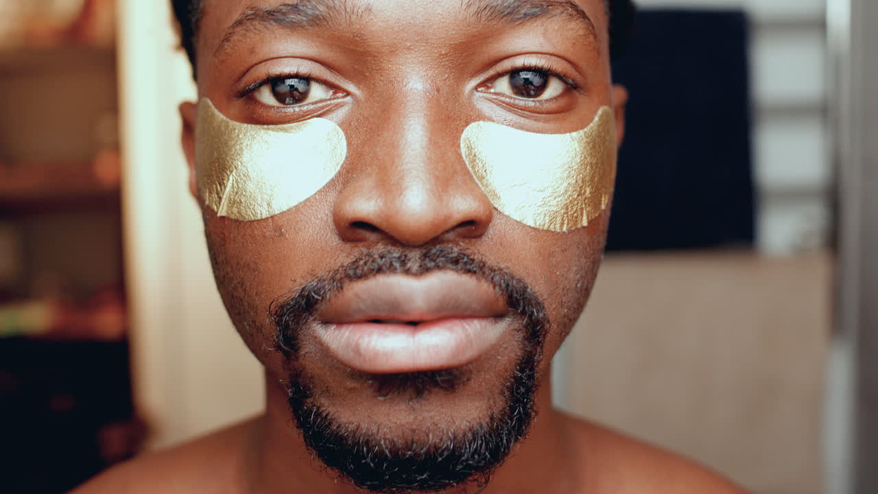 retrato de un joven negro aplicando parches debajo de los ojos en el baño