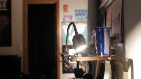 Clip-on-desk-lamp-lit-up-in-small-messy-room-close-up