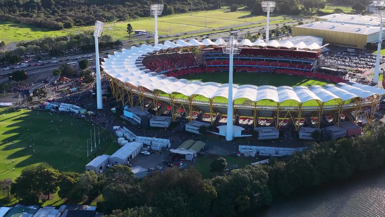 High-angle drone shot of a circular sports arena beside a river during golden hour.
