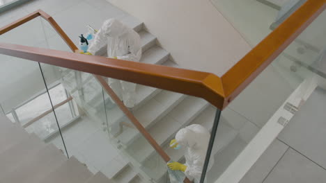 top view of two cleaning men wearing personal protective equipment cleaning stair railings inside an office building 2