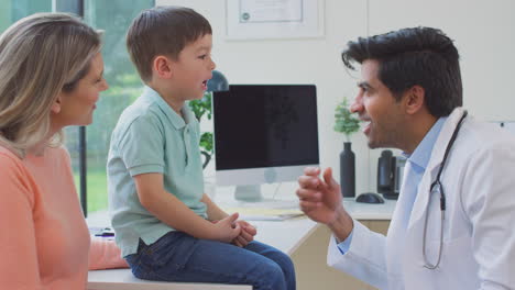 male doctor or gp wearing white coat examining boy looking at mouth and throat