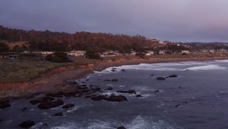 Aerial-low-close-up-shot-of-oceanfront-inns-lining-Moonstone-Beach-at-sunset-in-Cambria,-California