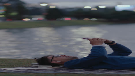 young man lying in city park and using smartphone