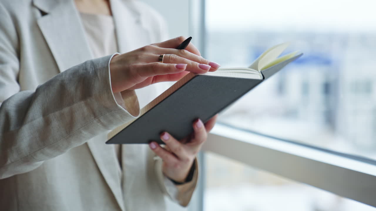 Unrecognizable woman holding a notebook in one hand and pen in another. Lady is taking notes into her book. Close up.