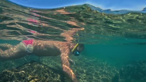 half underwater view of man with mask and snorkel fishing sea urchin in shallow water