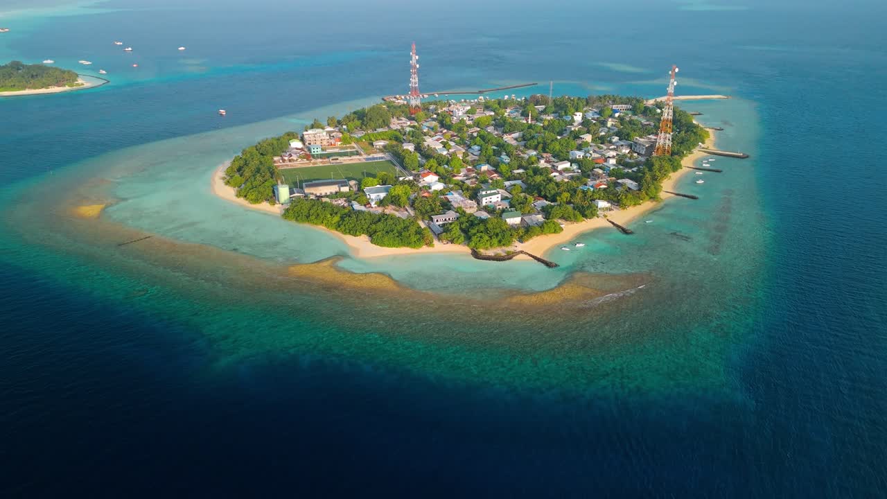 A stunning aerial drone view showcasing Rasdhoo Island surrounded by crystal-clear turquoise waters and vibrant coral reefs in the Maldives.