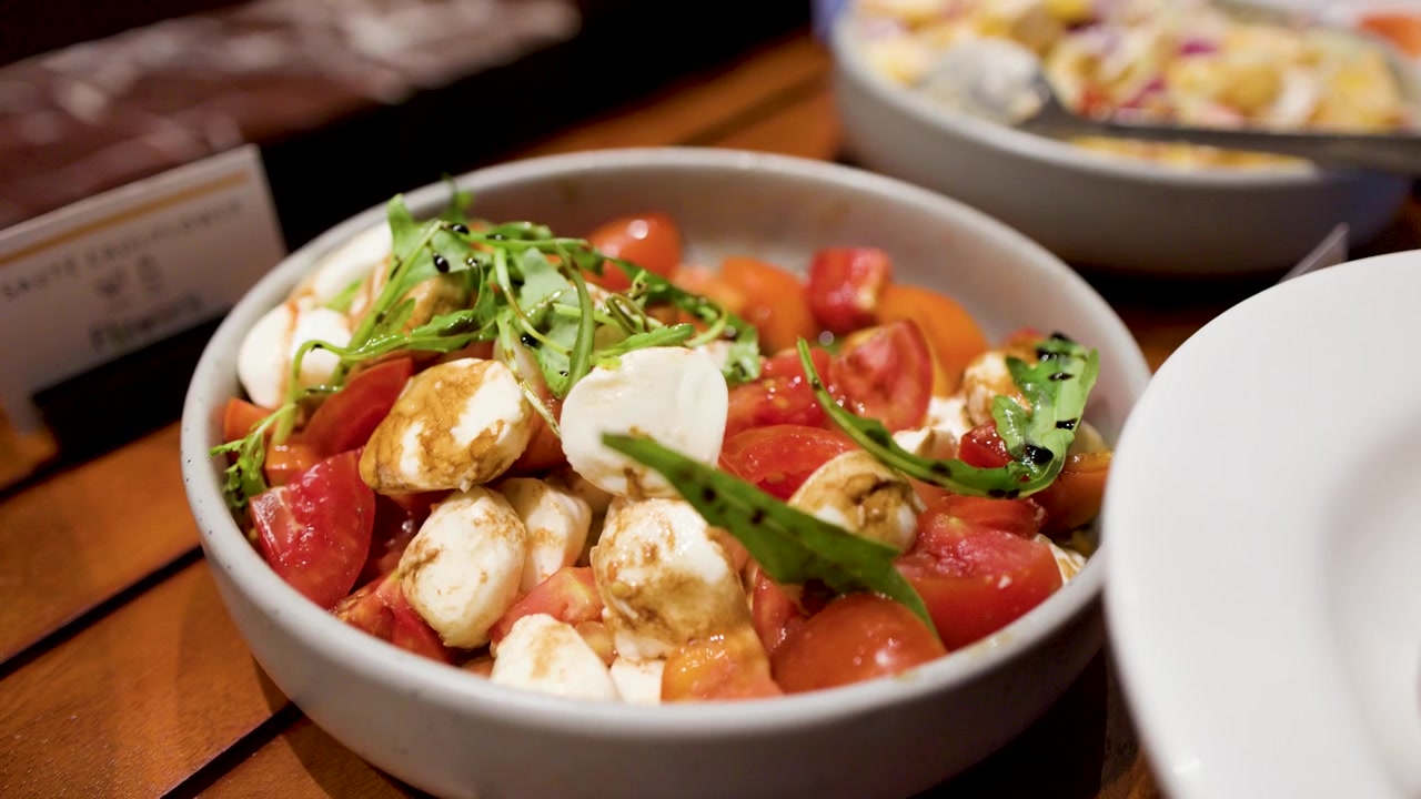 Un cucchiaio di metallo serve fresca insalata Caprese con mozzarella, pomodori e glassa balsamica a buffet