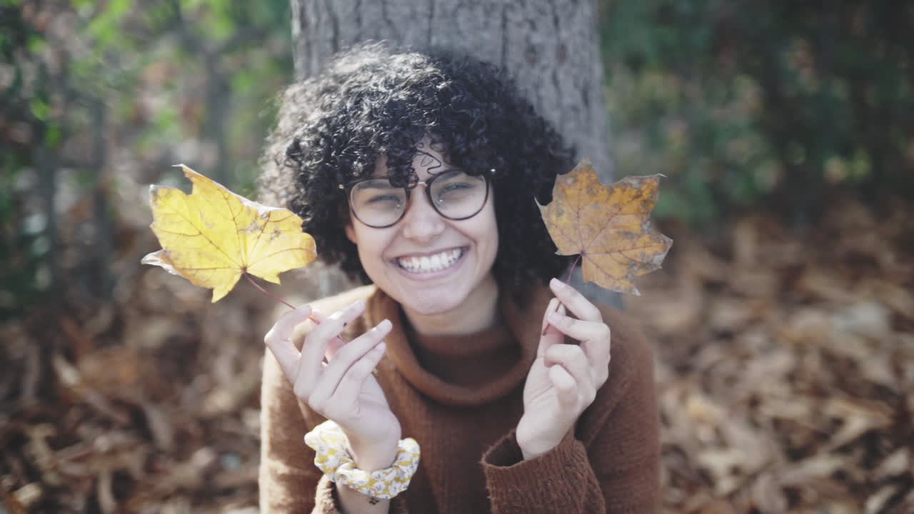 una chica tímida y tonta con rizos afro jugando con hojas secas de otoño