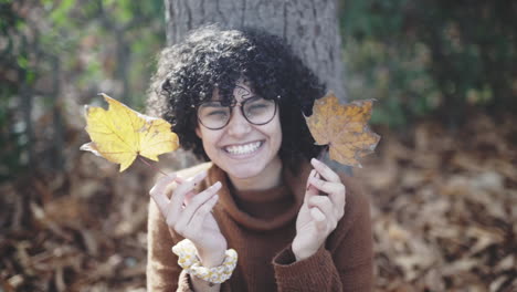 silly shy girl with afro curls playing with autumn dry leaves