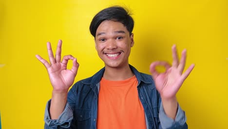 happy young asian man showing ok sign using fingers and make a move isolated on yellow background