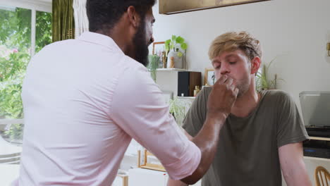 male gay couple at home in kitchen eating strawberries together