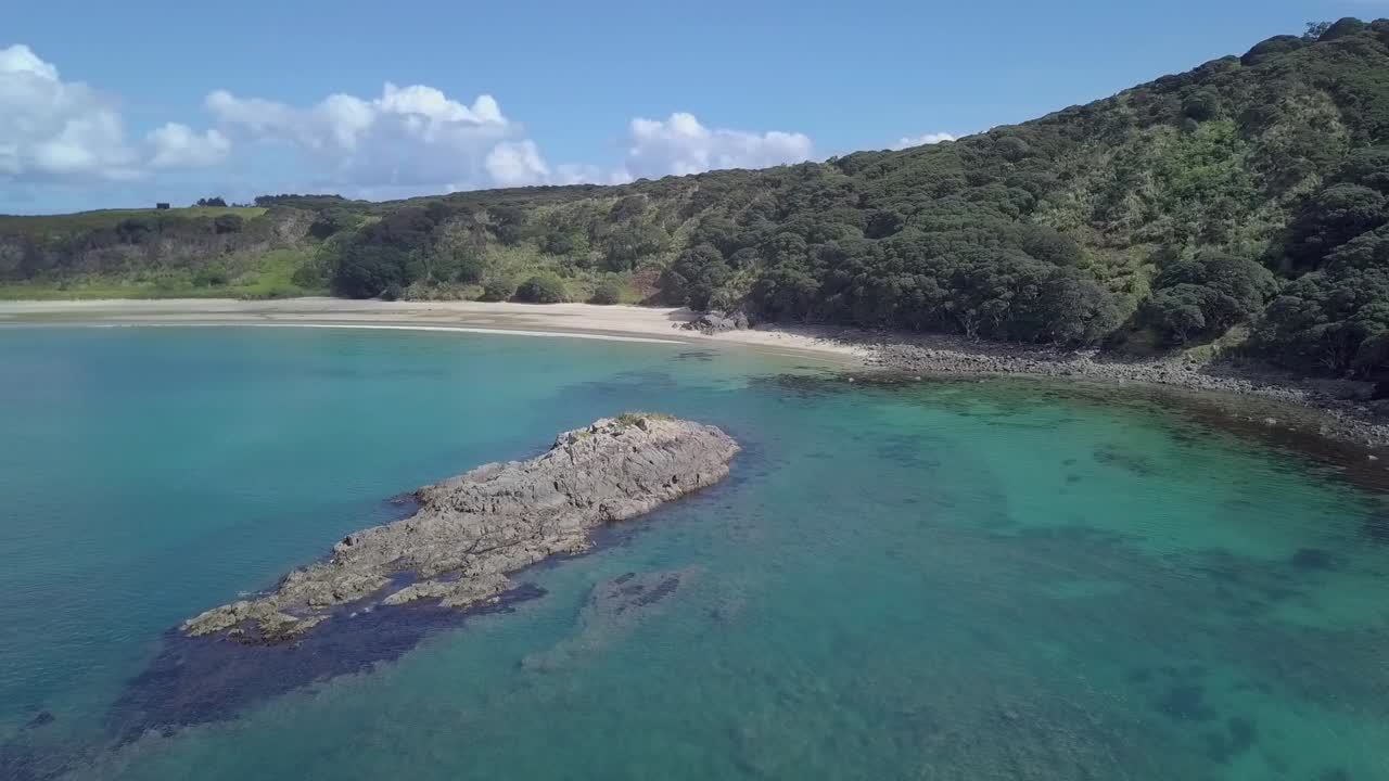 drone descendiendo sobre un islote rocoso hacia la playa de arena de la bahía de maitai en la península de karikari en nueva zelanda