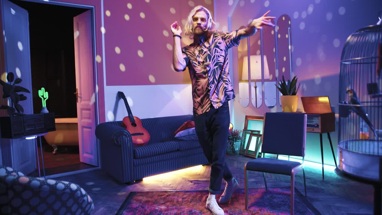 집에서 복고풍 파티에서 정력적으로 춤을 추는 헤드폰에 긴 머리를 가진 젊은 세련된 백인 남자