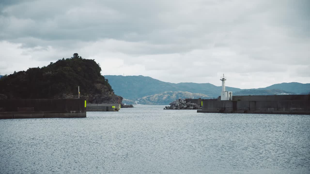 Beautiful view of the marina pier in Saikazaki, Japan with calm waters, mountains, and a lighthouse on a cloudy day
