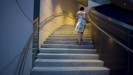 a-young-attractive-woman-in-a-flower-and-butterfly-dress-walks-up-the-stairs-at-a-leisurely-pace-then-speeds-up