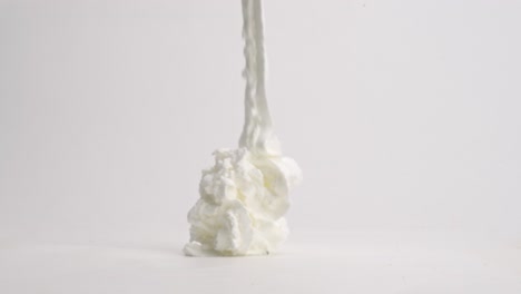 fresh, fluffy white whipped cream ribbons landing in pile on white table top in slow motion