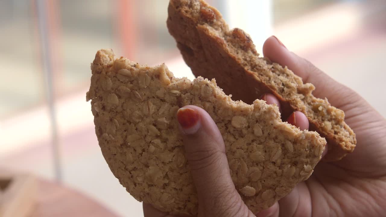 las manos de una mujer sostienen y rompen una gran galleta de avena