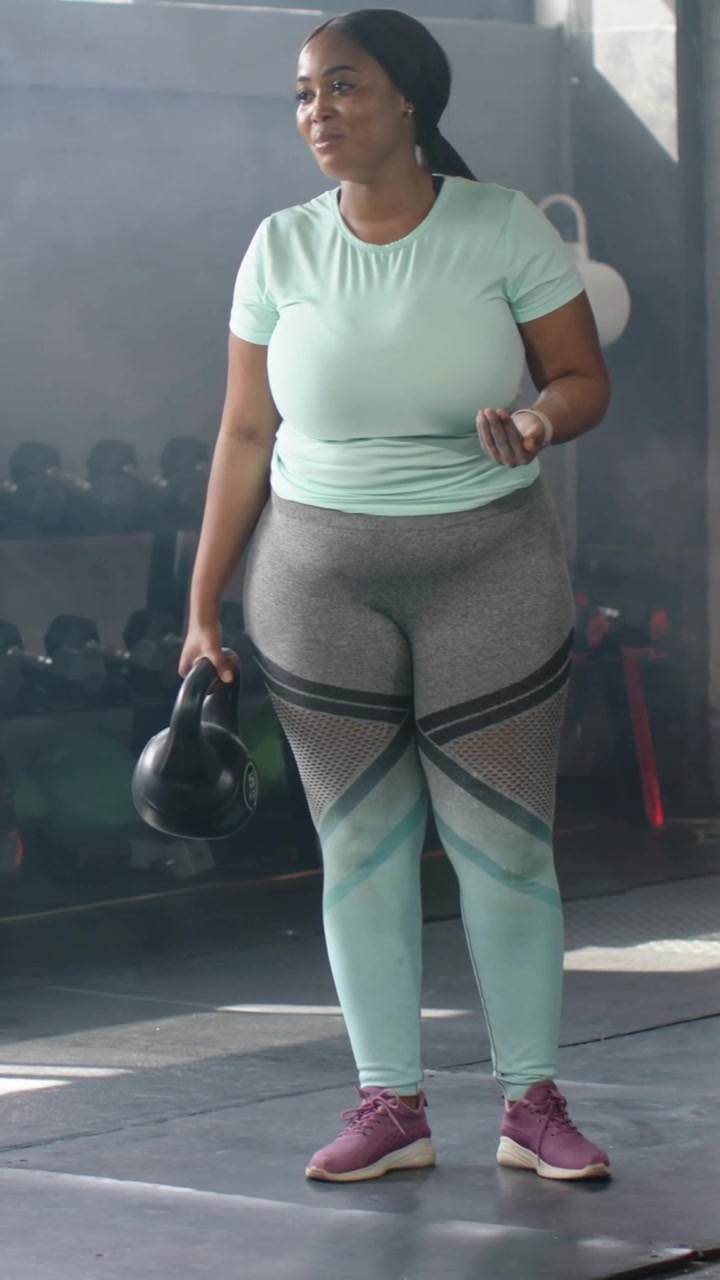 Video verticale: Donna con top color menta che riceve un segnale dall'allenatore, tiene un kettlebell e gesticola in palestra