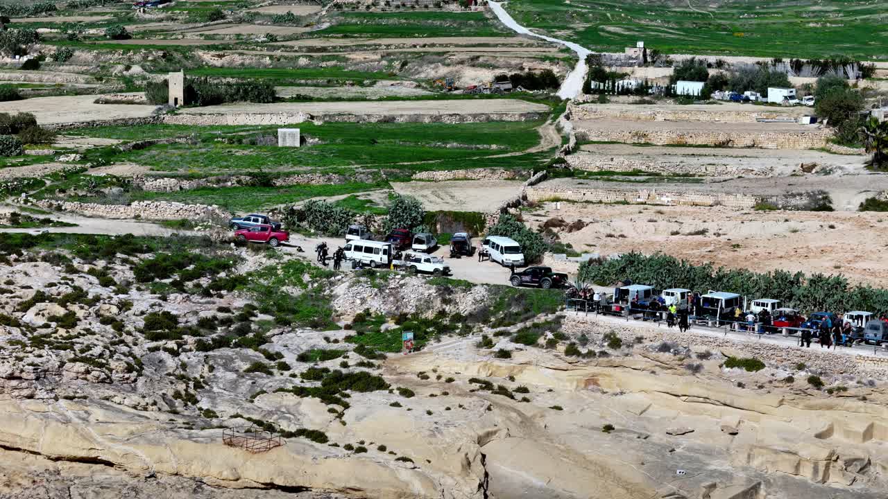 Gozo Malta'da, ilkbahar mevsiminde, parlak güneşli hava koşullarında, dağınık araçlar ve kırsal manzaralar içeren teraslı tarlaların ve kıyı kireçtaşı kayalıklarının panoramik yüksek açıdan görünümü.