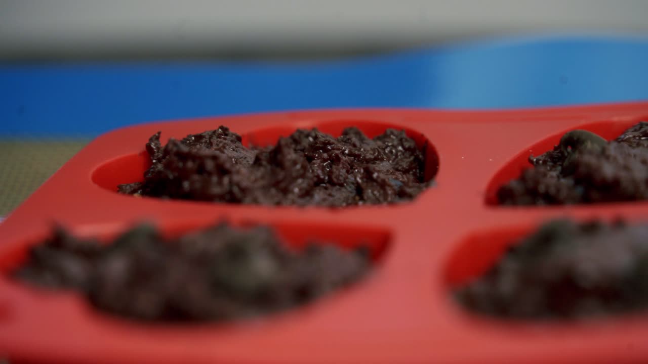 Primo piano: aggiunta di gocce di cioccolato a muffin di barbabietola al cioccolato in una teglia da forno per San Valentino, dolcetti a forma di cuore