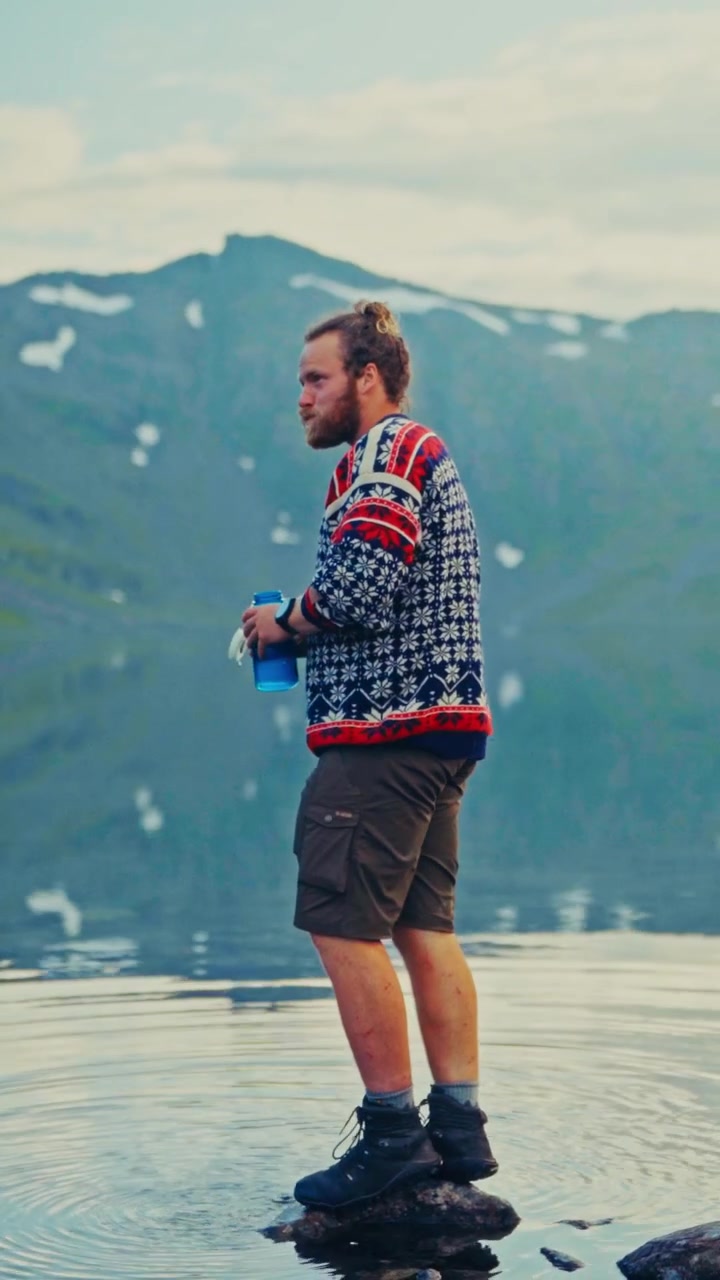 Un uomo sta in piedi su una roccia in un sereno lago di montagna, mentre beve immerso in un paesaggio mozzafiato - Scatto verticale.