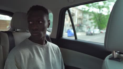 handsome young black man rides on back seat of a car, looks around in wonder out of the window. big city view reflected in window. wearing white casual shirt