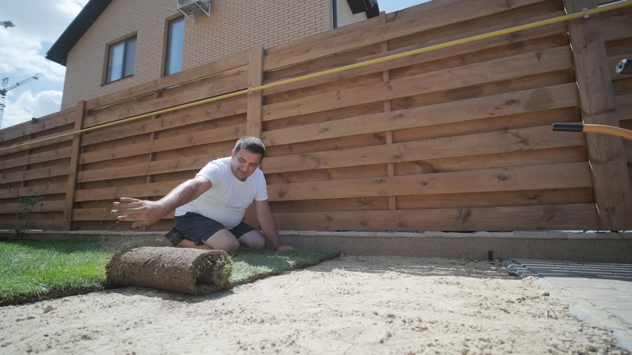 человек, укладывающий траву в заднем дворе для установки газона и ландшафтного проекта, сосредоточенного на улучшении дома и обслуживании на открытом воздухе для свежего, зеленого газона в жилом дворе