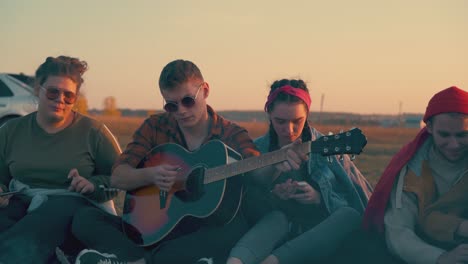 young man plays guitar to friends resting in tourist camp