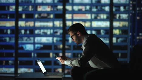 Office-Building-with-Businessman-Using-Mobile-Phone-and-Standing-by-the-Office-Window.-Man-working-in-modern-office-late-at-night.-Busy-caucasian-manager-at-work-with-mobile-telephone.