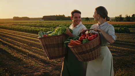 couple carrying baskets of fresh vegetables in a field at sunset