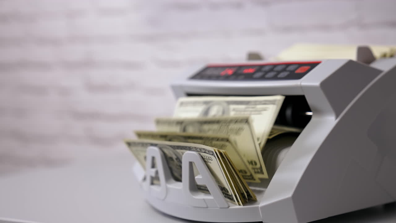 Bank automatic equipment for calculation paper currency. Currency counting machine counting dollar bills. Female worker taking out a bundle of one hundred usd from automatic machine. Side view.