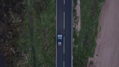 a top down moving drone shot of a road, that has a car come into frame from the bottom and exiting out of the top