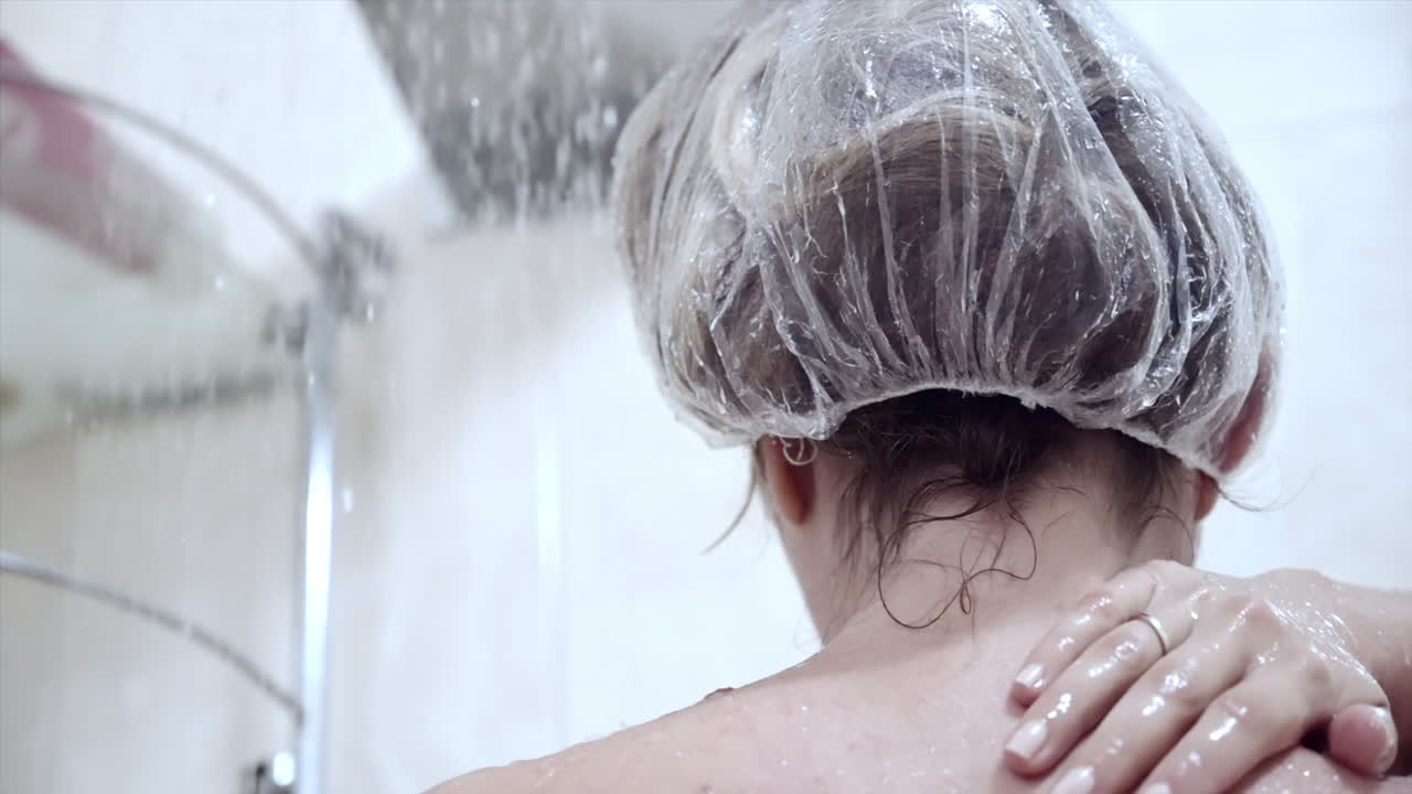 Close up of a woman showering with a shower cap on her head