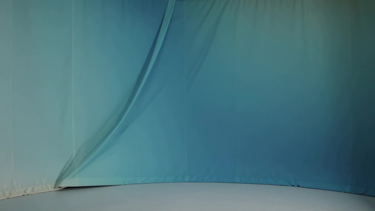 Pulling overhead rigging dragging blue curtain upward in studio under soft lighting, revealing fold