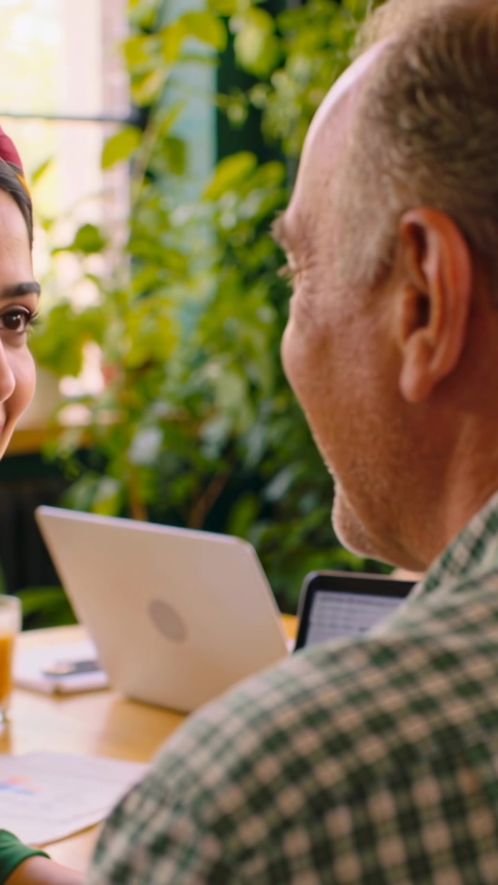 Vertical video: Smiling woman in green top starting warm chat as man nodding at cafe, laptop open