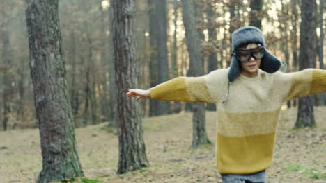 pequeño niño caucásico soñador de ser piloto divirtiéndose y corriendo en círculos en el bosque con las manos abiertas