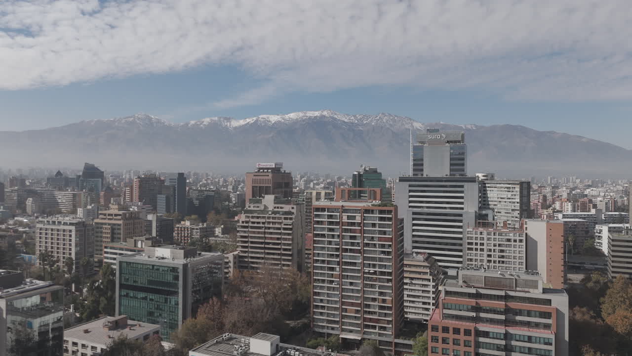Upwards drone shot of Santiago de Chile in South America watching over the skyscrapers and big buildings with snowy mountains in the background on bright but cloudy day LOG