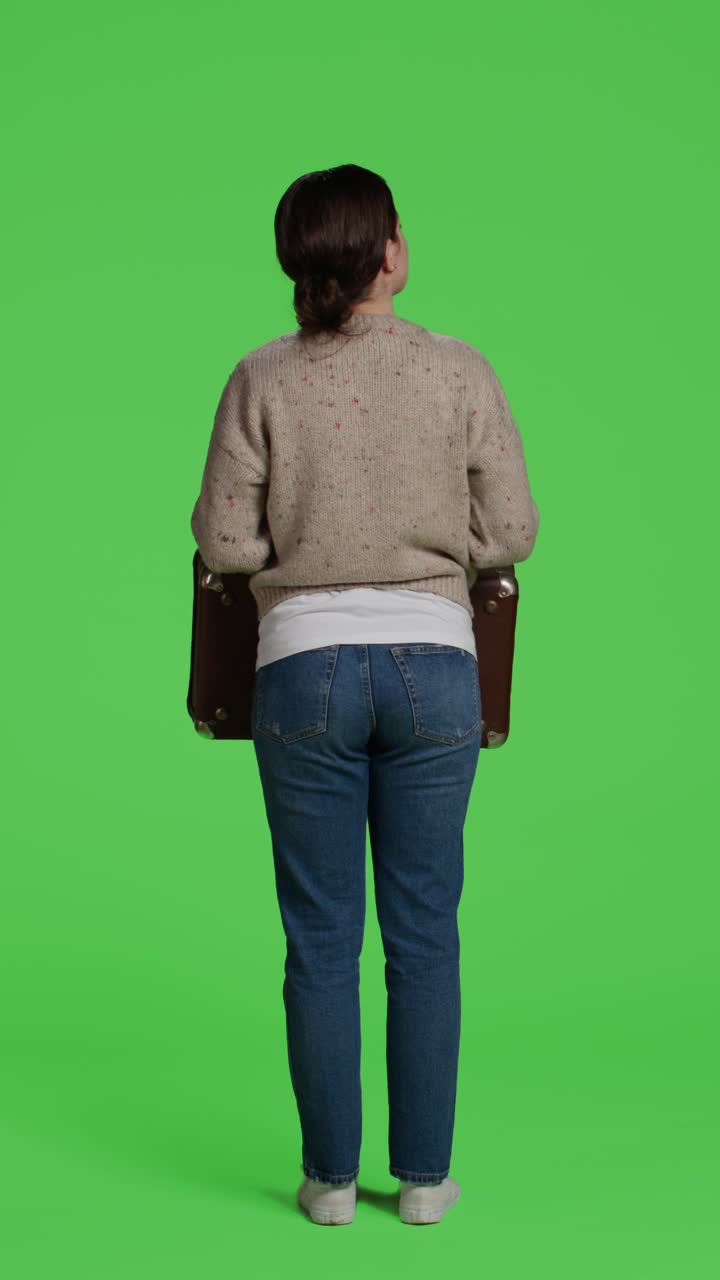Vertical video: Back view of casual person carrying suitcase in studio