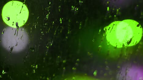 gotas de lluvia nocturna en la ventana sucia con luces de bokeh verdes parpadeantes en el fondo