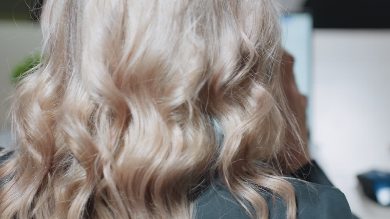 Behind view of woman holding takeaway coffee cup near laptop while working in bright office setting, hand resting near mouse, screen open to blank document