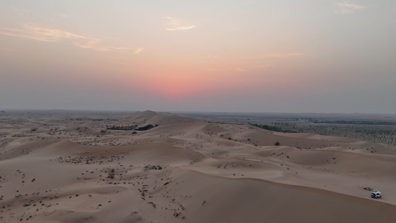 Desert sand dunes at sunset with sparse shrubs and distant horizon in Abu Dhabi, aerial pullback over campers