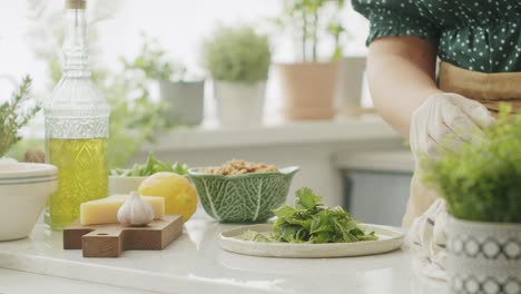 anonymous woman tearing green basil leaves during cooking in kitchen
