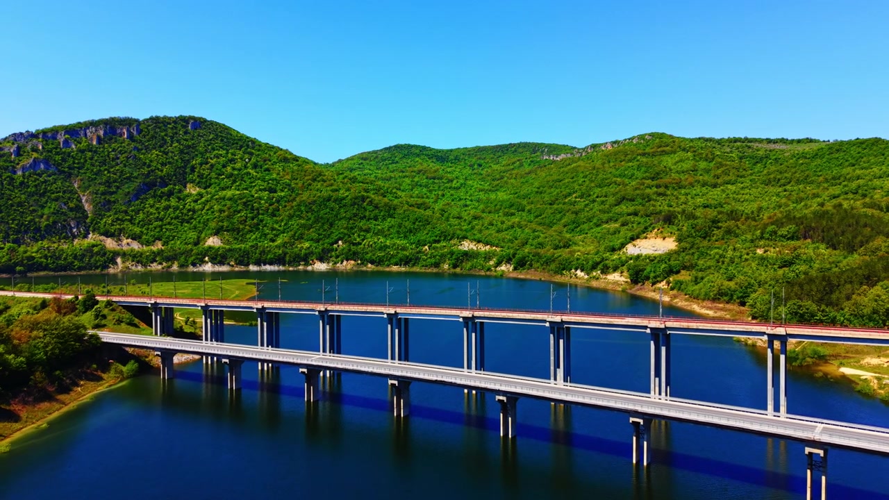 Broer spænder over vand, Bulgarien. Sideperspektiv af parallelle jernbane- og vejbroer, der strækker sig over et dybt reservoir flankeret af skovklædte skråninger.