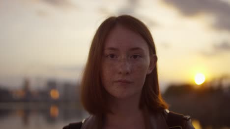 retrato de jovem com cabelo ruivo e sardas olhando para a câmera ao pôr do sol