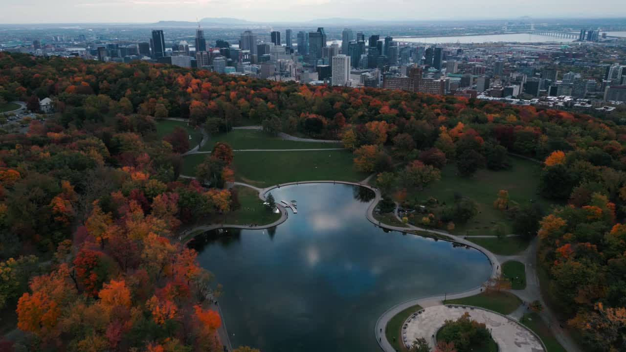 Drone shot over Montreal city from the parc Mont Royal and the "lacs aux castors" during fall season with the trees and lake in the foreground and the buildings in the background
