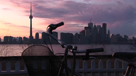 a bicycle is parked near the coastline of lake ontario with the skyline of toronto in the background