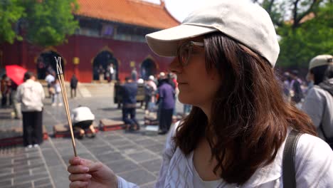 tourist woman holds incense sticks at lama temple in beijing, focusing on the buddhist ritual