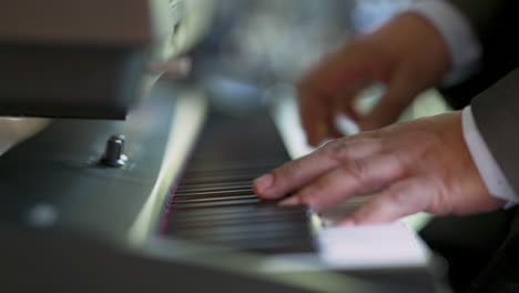 a side shot of a man's hand playing a black electric piano while wearing a suit.