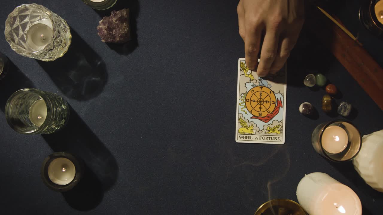 toma aérea de una persona que da una lectura de cartas del tarot colocando la rueda de la fortuna en la mesa