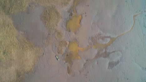 drone flight of the bank of an estuary looking down and passing over two boats. following the sediment along the waters edge